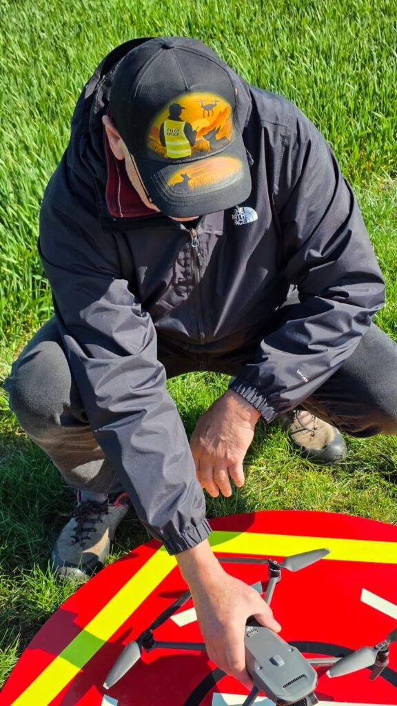 Helfer bereitet Drohne im Feld zur Rehkitzrettung vor und trägt KitzCaps Cap